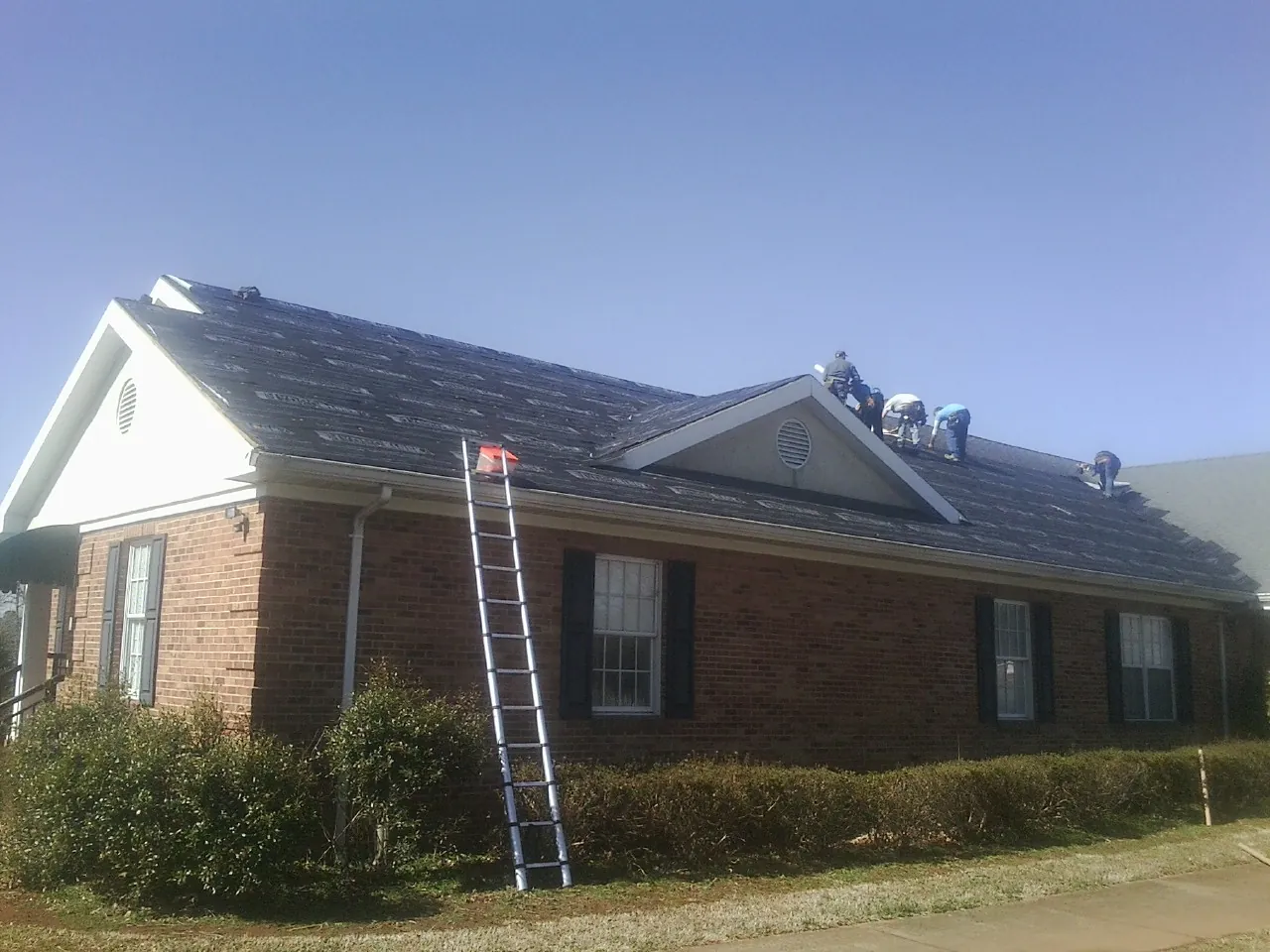 Crew tearing shingles off a brick ranch roof with a ladder set — Emergency Roof Repair work by our crew in Totowa