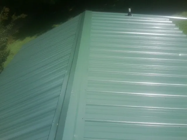 New green metal panels meeting at the ridge of a roof — Flat Roof Repair work by our crew in Totowa