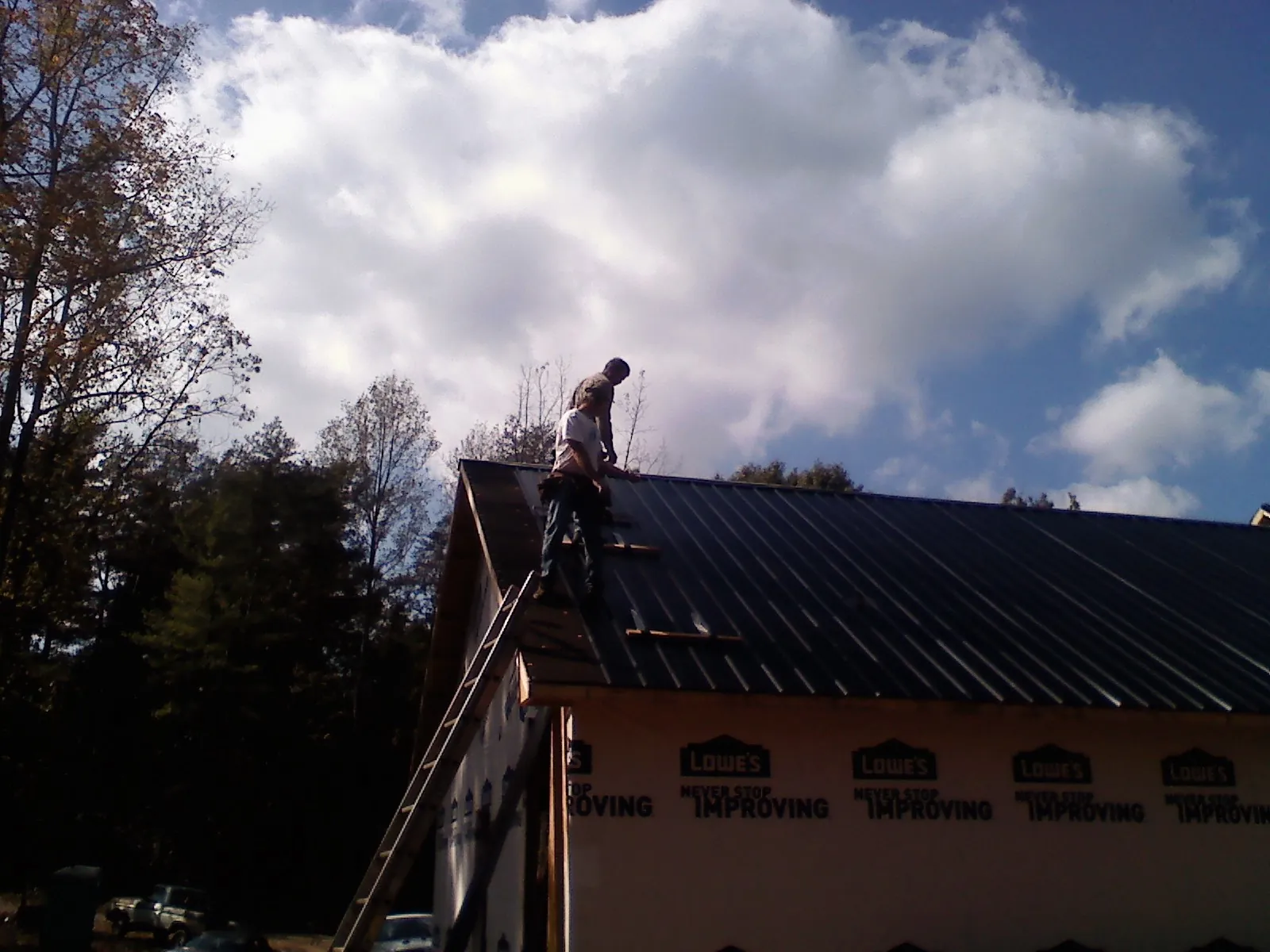 Roofer fastening dark metal panels high against a cloudy sky, from a Roof Inspection job in Totowa