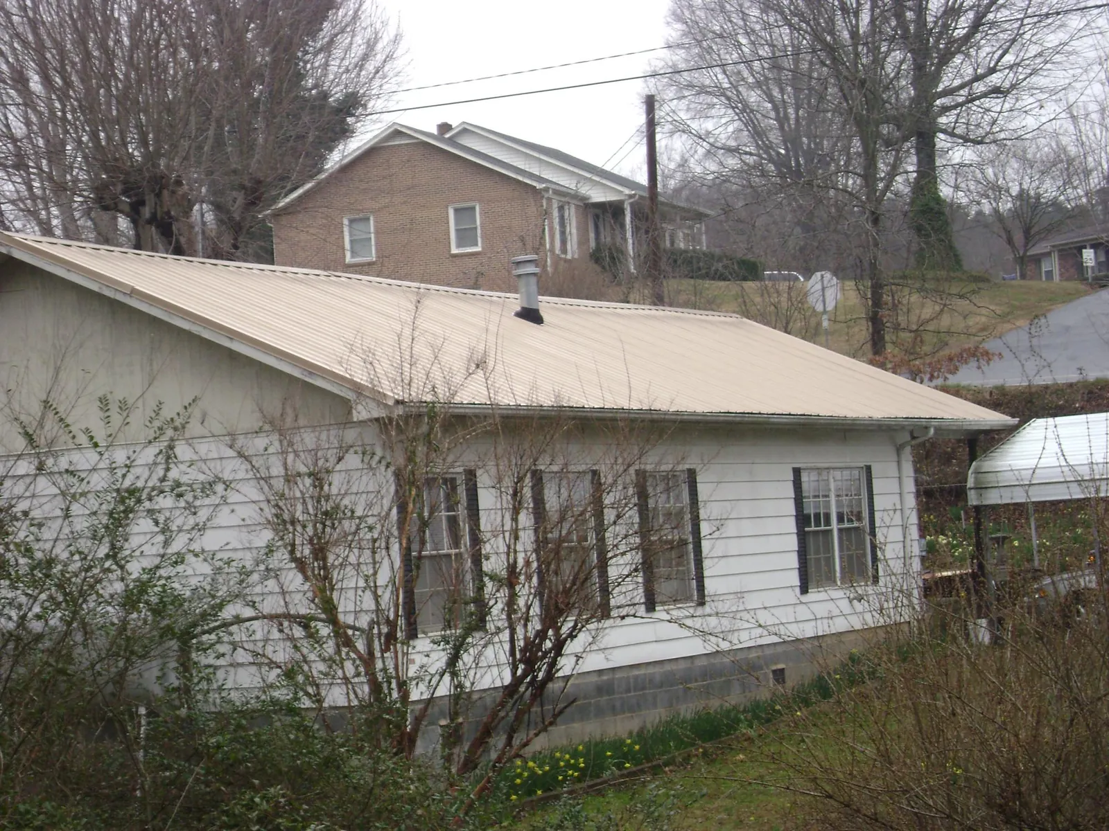 Tan metal roof on a white sided house set into a hillside — Commercial Roofing by Roofing Brothers in Totowa